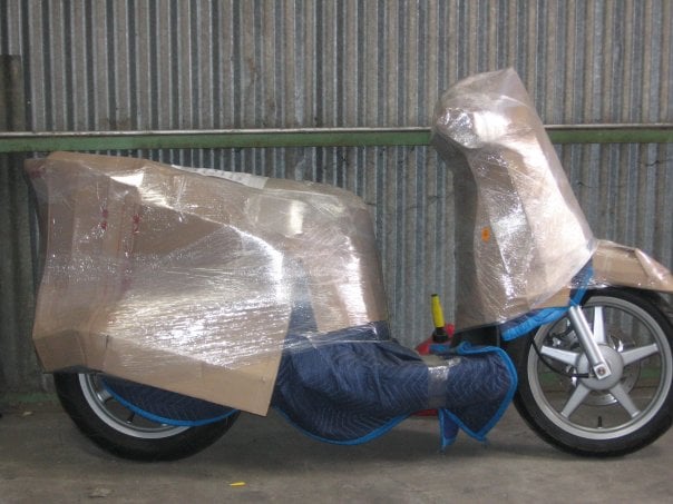 Motor scooter wrapped in moving blankets, cardboard and stretch wrap, ready to load
