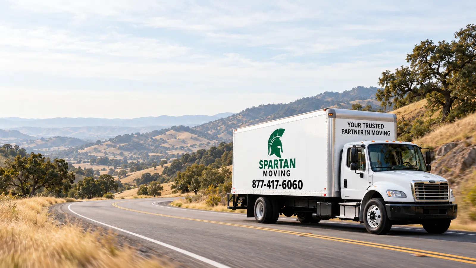 Spartan Moving box truck driving a winding two-lane road through golden California hills